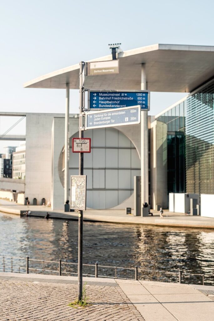 Street signs point towards destinations near a modern building.